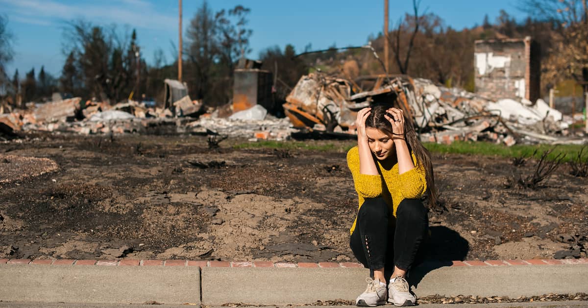 Distraught young woman sitting outside her destroyed home after natural disaster | ATI Restoration
