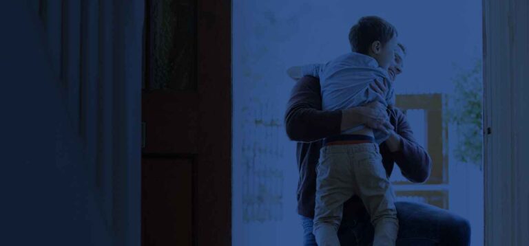A father embraces his son in a heartfelt hug at the doorway.