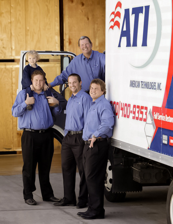 Group photo of five men and a young child standing in front of an American Technologies, Inc. moving truck.