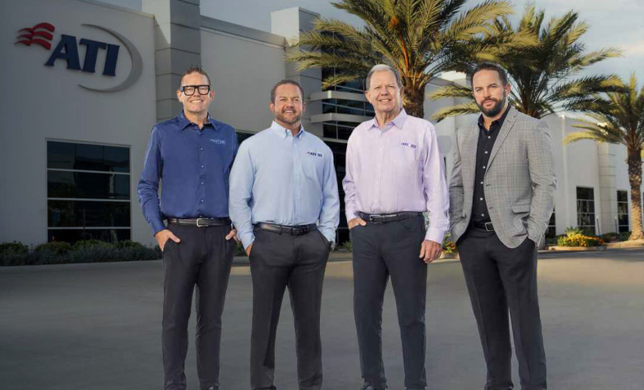 Four men in business attire stand in front of the ATI company building.